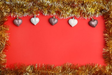 Photo of Frame of shiny golden tinsel and Christmas baubles on red background, flat lay. Space for text