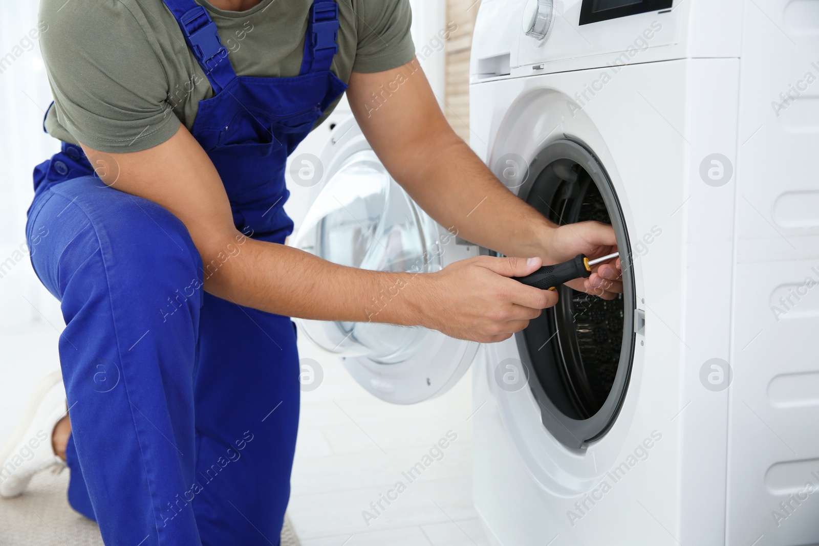 Photo of Young handyman fixing washing machine, closeup. Laundry day