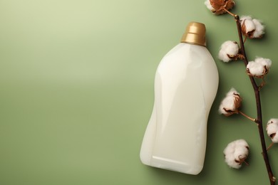 Photo of Bottle of fabric softener and fluffy cotton flowers on light green background, flat lay. Space for text
