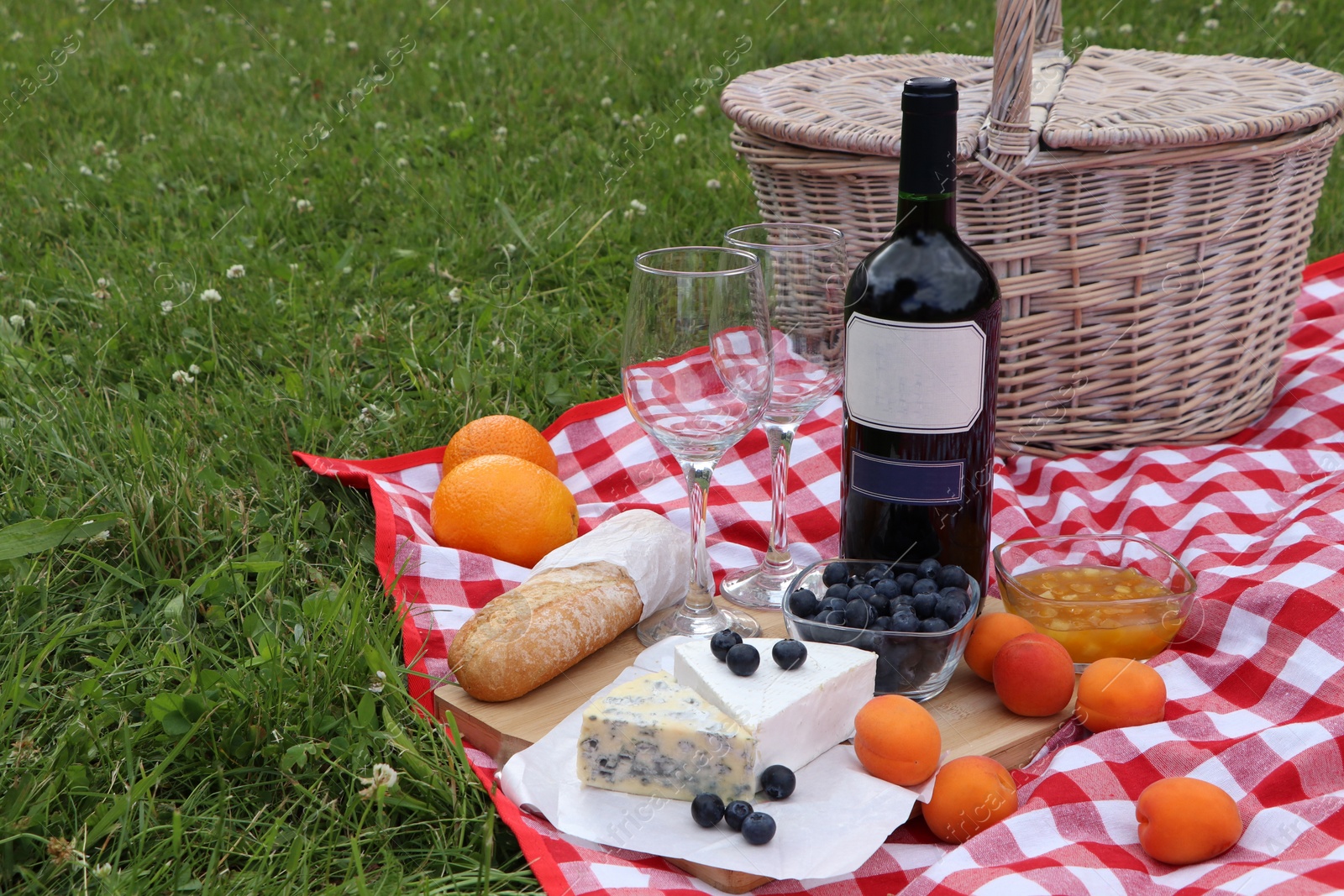 Photo of Picnic blanket with delicious food and wine outdoors on summer day