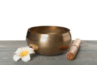 Photo of Golden singing bowl, mallet and flower on grey wooden table against white background