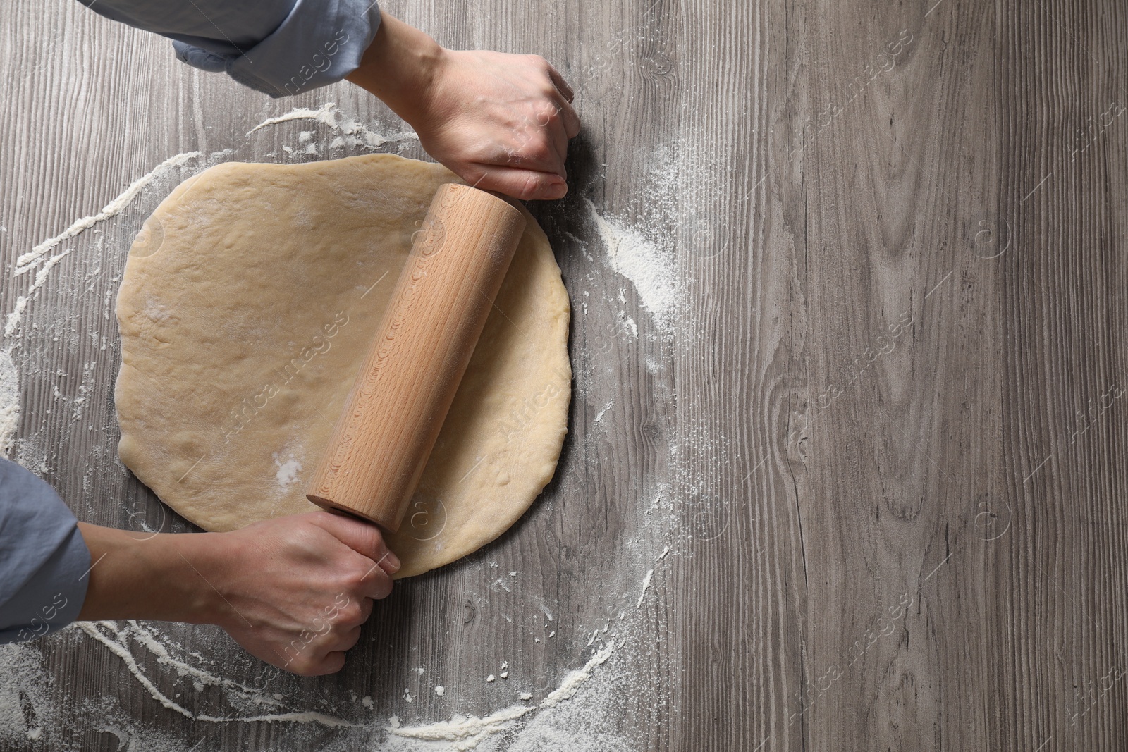 Photo of Woman rolling raw dough at wooden table, top view. Space for text