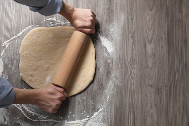 Woman rolling raw dough at wooden table, top view. Space for text