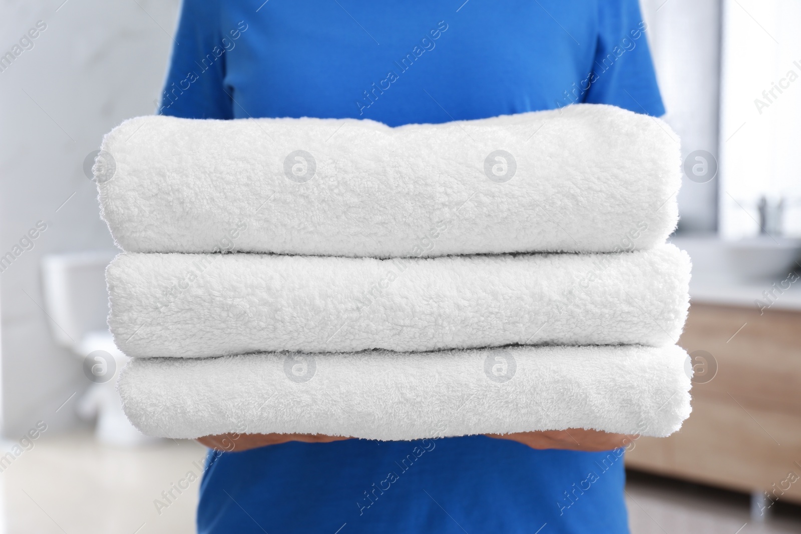 Photo of Woman holding fresh towels in bathroom, closeup