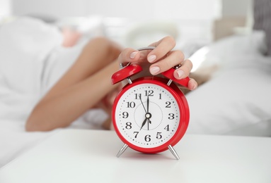 Woman turning off alarm clock in bedroom