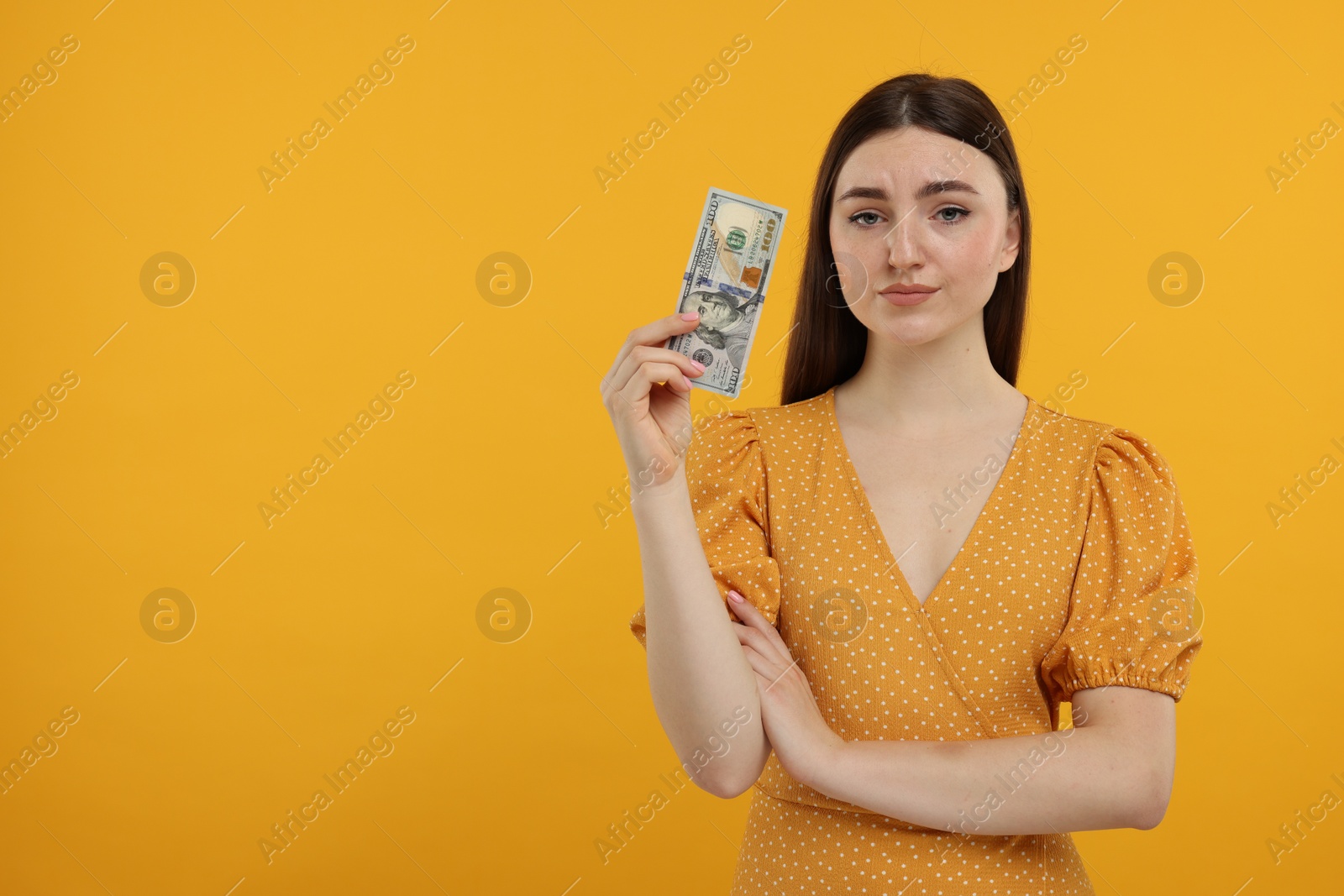 Photo of Sad woman with dollar banknote on orange background, space for text