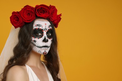 Photo of Young woman in scary bride costume with sugar skull makeup and flower crown on orange background, space for text. Halloween celebration