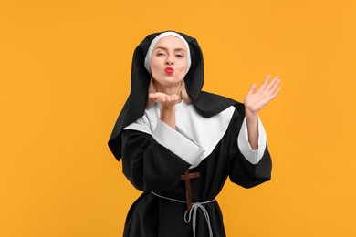 Photo of Woman in nun habit blowing kiss against orange background