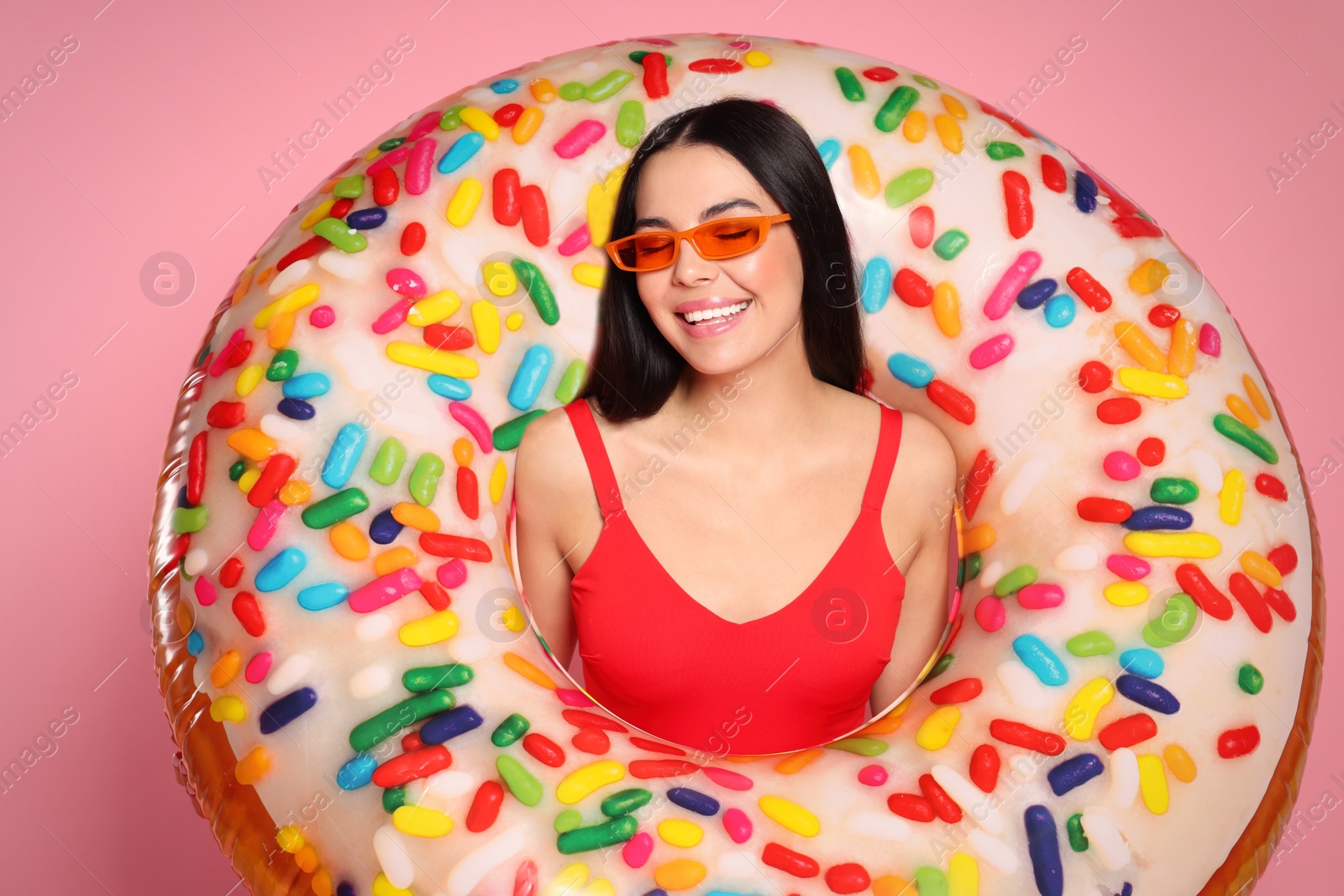 Photo of Young woman with stylish sunglasses holding inflatable ring against pink background