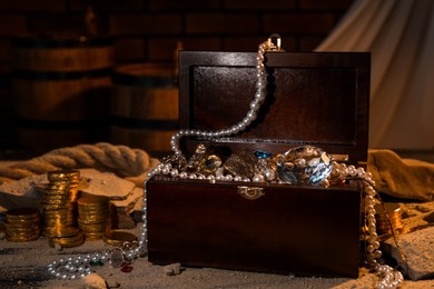 Photo of Chest with treasures, golden coins and scattered sand on table