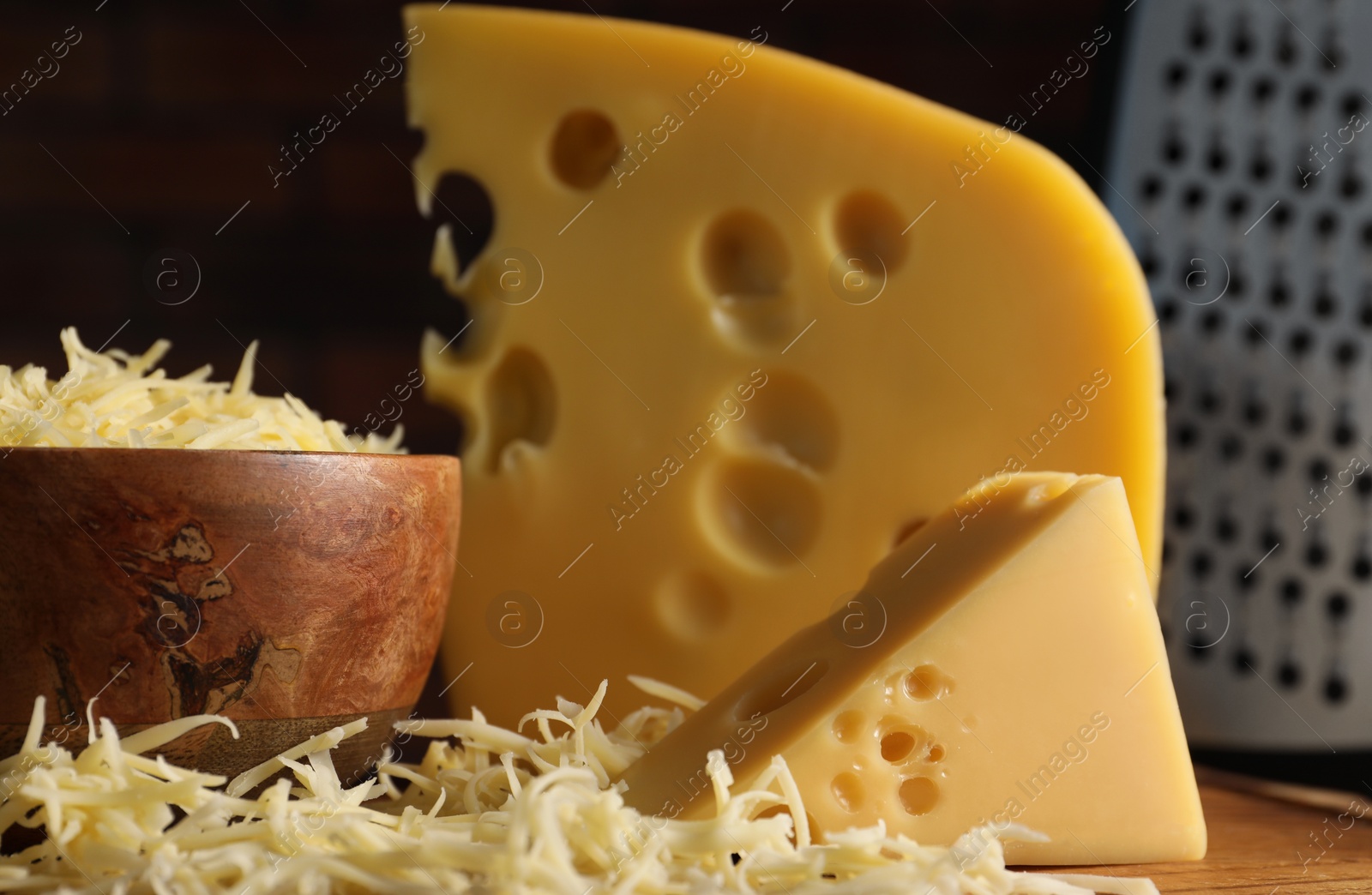 Photo of Grated and cut cheese on wooden board, closeup