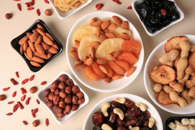 Bowls with dried fruits and nuts on beige background, flat lay