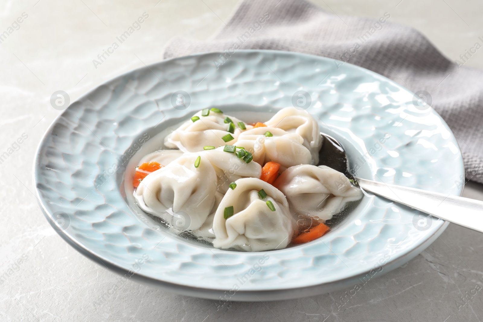 Photo of Plate of tasty dumplings in broth with spoon on grey marble table