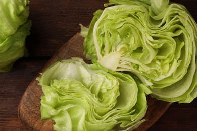 Photo of Board with fresh halves of iceberg lettuce head on wooden table, flat lay