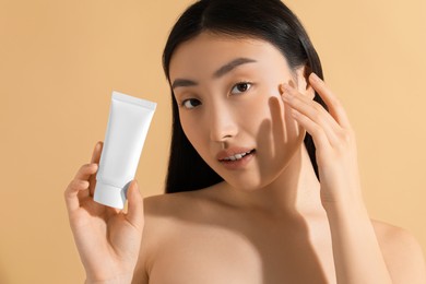 Photo of Beautiful young woman holding sun protection cream on beige background