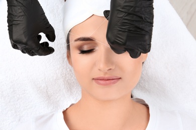 Photo of Young woman having professional eyebrow correction procedure in beauty salon