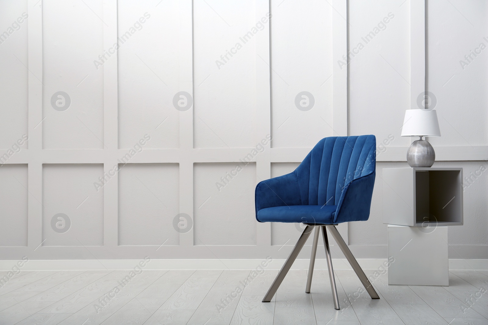 Photo of Modern blue armchair and lamp near white wall indoors. Space for text