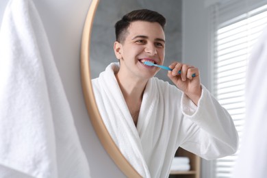 Man brushing his teeth with toothbrush near mirror in bathroom