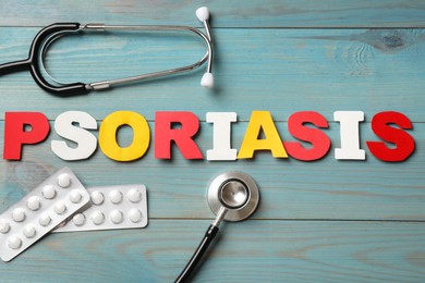 Photo of Word Psoriasis made of paper letters, stethoscope and pills on light blue wooden table, flat lay