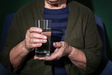 Poor senior woman with glass of water on color background, closeup