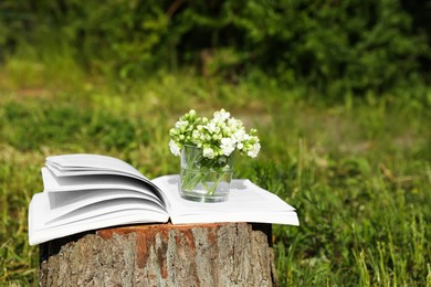 Photo of Open book and glass with flowers on tree stump outdoors