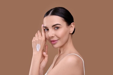 Photo of Beautiful woman with smear of body cream on her hand against light brown background