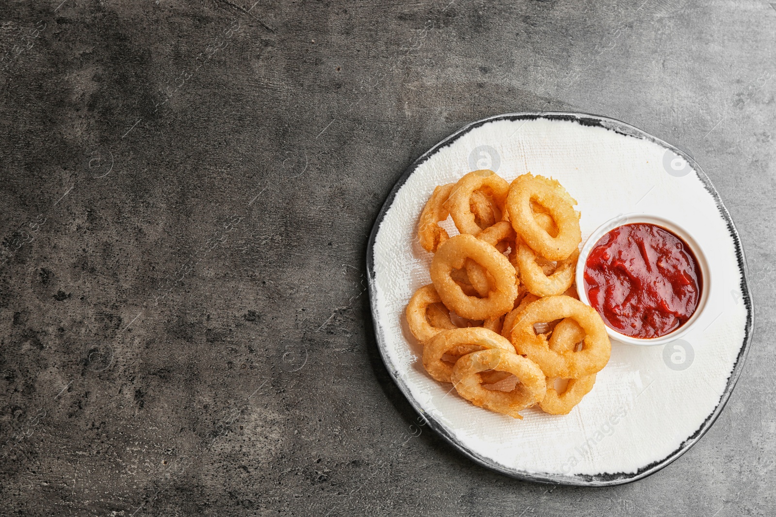 Photo of Plate with tasty onion rings and sauce on table, top view