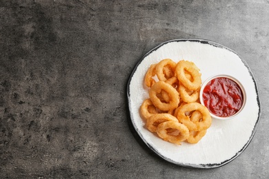 Plate with tasty onion rings and sauce on table, top view