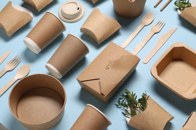 Photo of Eco friendly food packaging. Paper containers, tableware and green twigs on light blue background