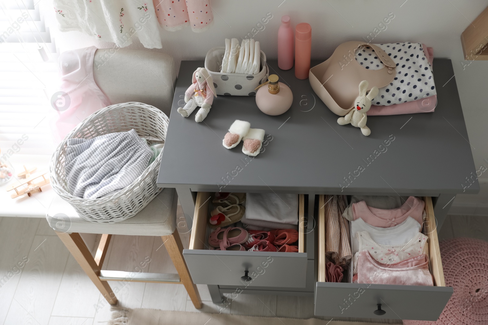 Photo of Open cabinet drawers with baby shoes and clothes in child room