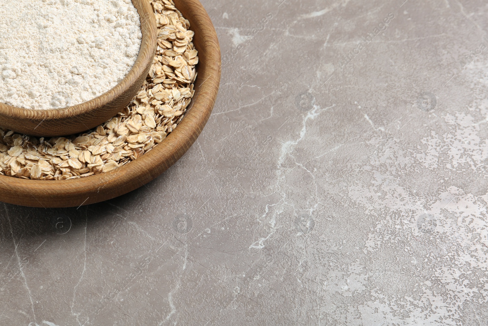 Photo of Bowls with oat flour and flakes on grey background. Space for text