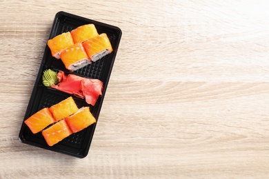 Photo of Tasty sushi rolls in box on wooden table, top view with space for text. Food delivery