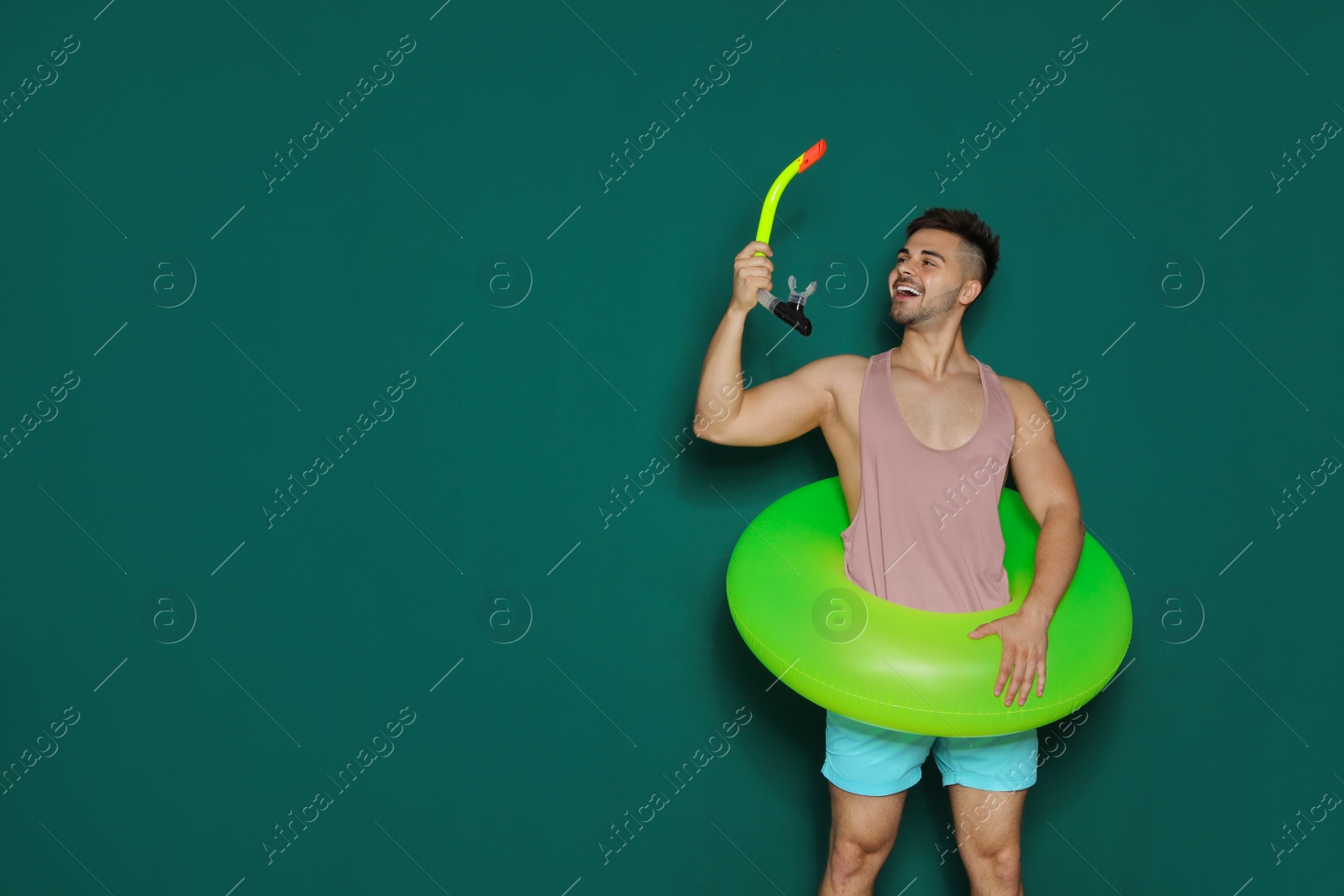 Photo of Funny young man with bright inflatable ring on dark green background, space for text