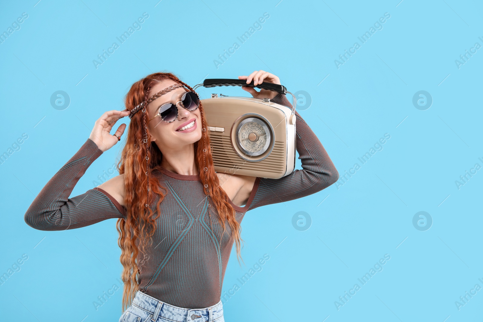 Photo of Stylish young hippie woman with retro radio receiver on light blue background