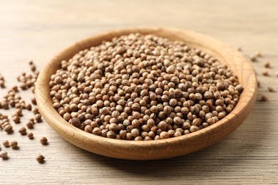 Photo of Dried coriander seeds in bowl on wooden table, closeup