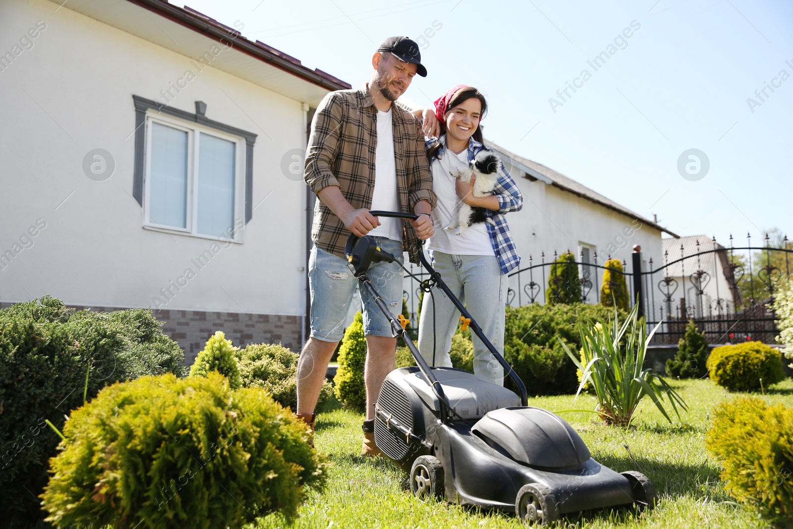 Photo of Happy couple spending time together while cutting green grass with lawn mower in garden