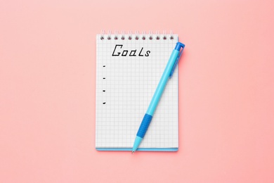 Photo of Notebook with goal list and pen on pink background, top view