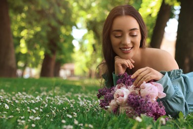 Photo of Beautiful woman with bouquet of spring flowers on green grass in park, space for text