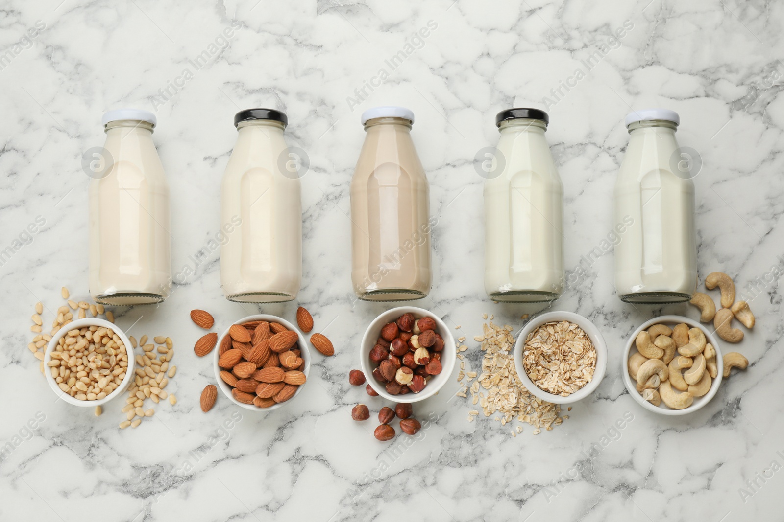 Photo of Different vegan milks and ingredients on white marble table, flat lay