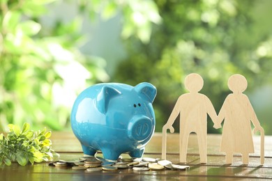 Photo of Pension savings. Figure of senior couple, piggy bank, coins and green twig on wooden table outdoors