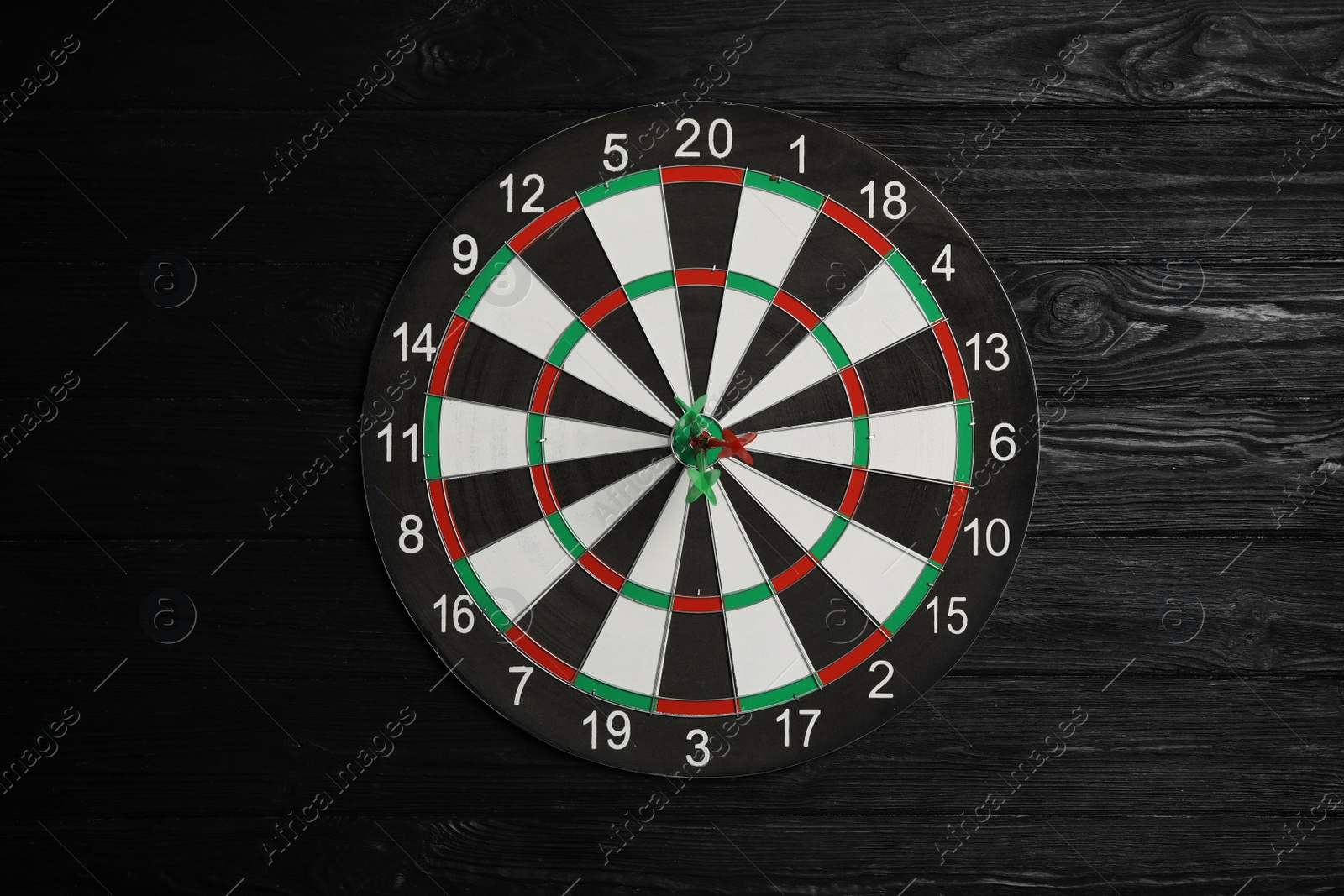 Photo of Dart board with color arrows on black wooden background, top view