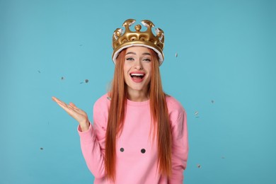 Beautiful young woman with inflatable crown under falling confetti on light blue background