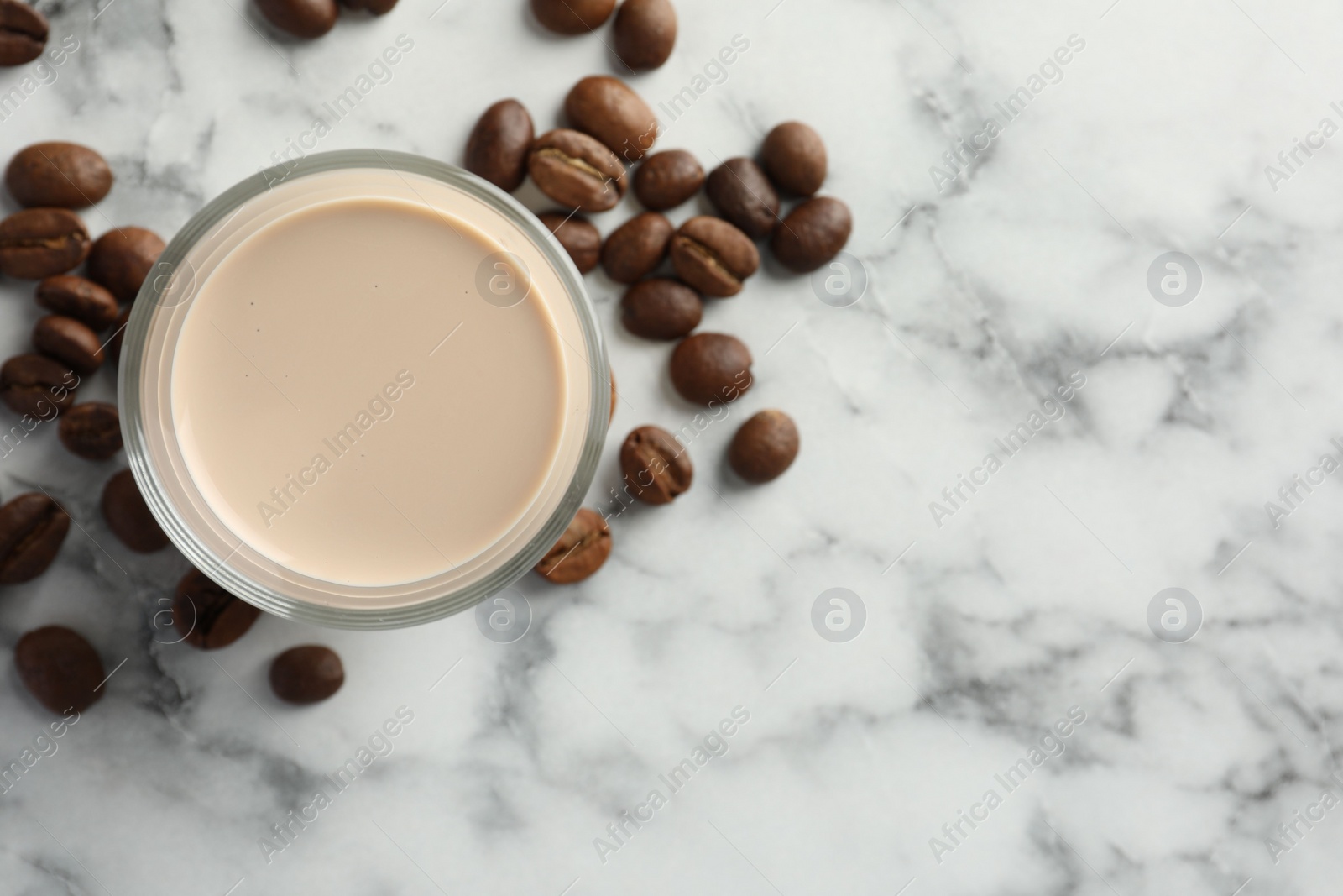 Photo of Coffee cream liqueur in glass and beans on white marble table, top view. Space for text