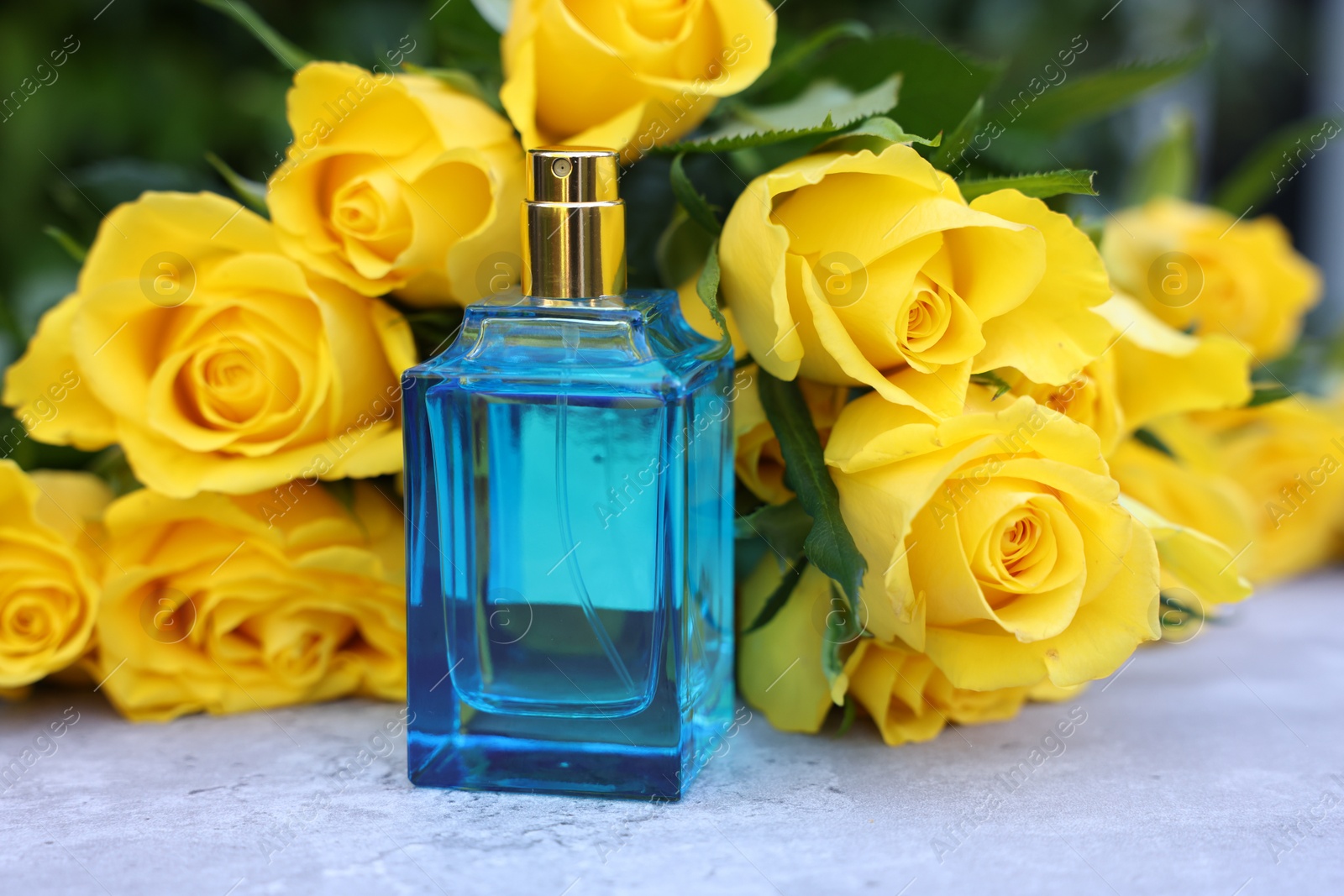 Photo of Perfume and beautiful bouquet of yellow roses on light table, closeup