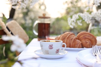 Stylish table setting with tea and croissants in spring garden