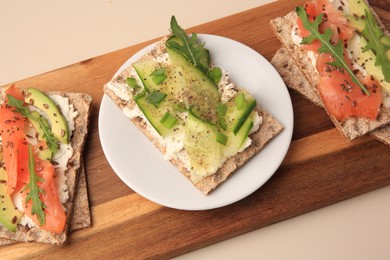 Photo of Fresh crunchy crispbreads with cream cheese, cucumber, green onion, salmon and arugula on beige table