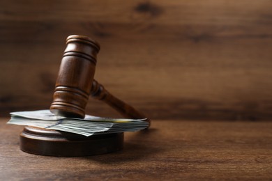 Photo of Law gavel with stack of dollars on wooden table, closeup. Space for text