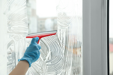 Photo of Woman cleaning window with squeegee indoors, closeup