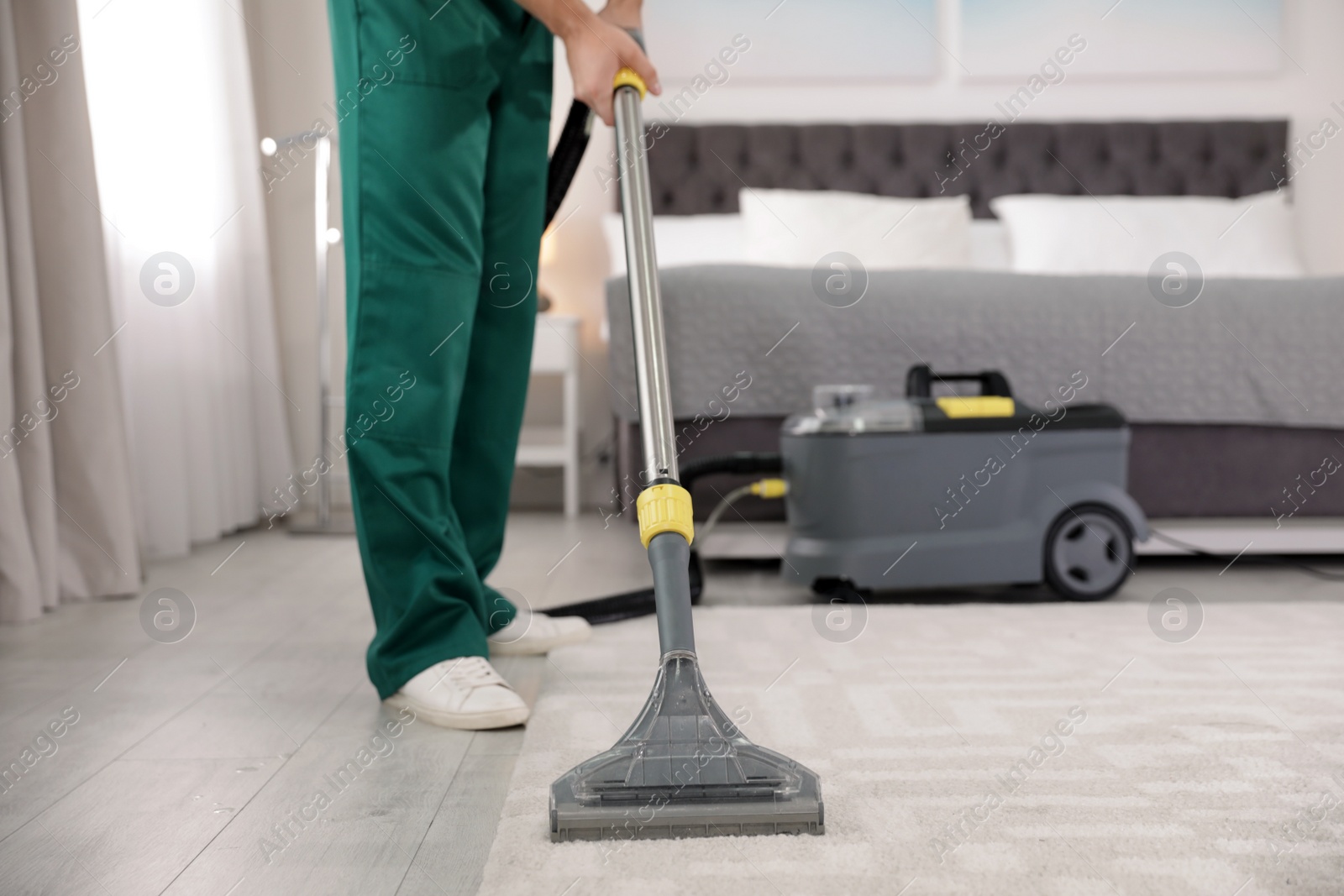 Photo of Professional janitor removing dirt from carpet with vacuum cleaner in bedroom, closeup. Space for text