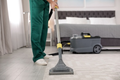 Photo of Professional janitor removing dirt from carpet with vacuum cleaner in bedroom, closeup. Space for text